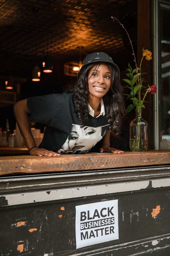 Businesswoman smiling behind a bar counter at a black-owned business promoting community support.