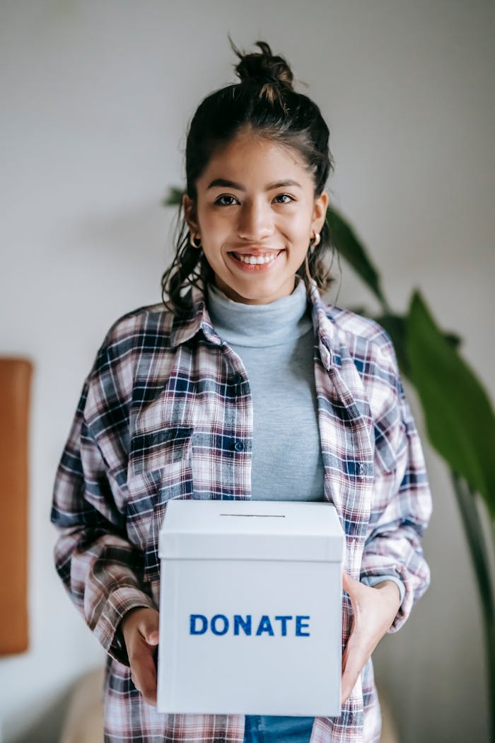 Cheerful woman holding a box labeled 'Donate' indoors, symbolizing charity and kindness.